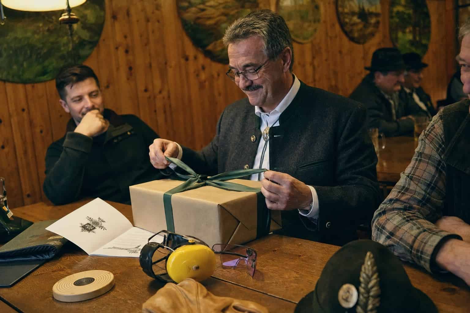 Schützen an der Tafel, einer öffnet ein verpacktes Geschenk